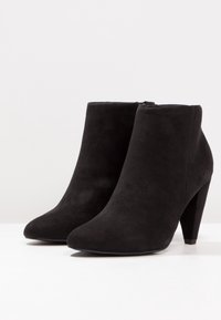 Mustat mokkasiin ankle-botit, joissa on terävä nenä ja korkea stiletto-korko. Sivuvetoketju helpottaa pukemista. Sileä pinta ja tyylikäs muotoilu.