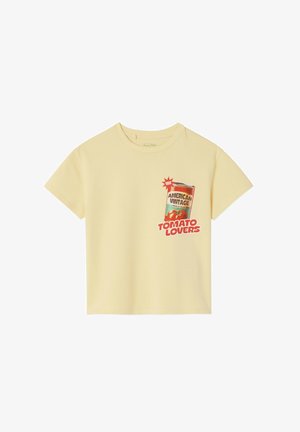Geel katoenen T-shirt met een afbeelding van een tomatenblikje. De tekst luidt "AMERICAN VINTAGE" en "TOMATO LOVERS" in rood en zwart. Korte mouwen.