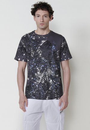 Camiseta negra y azul con patrón, de cuello redondo y mangas cortas, que presenta gráficos abstractos y salpicaduras sobre un fondo texturizado.