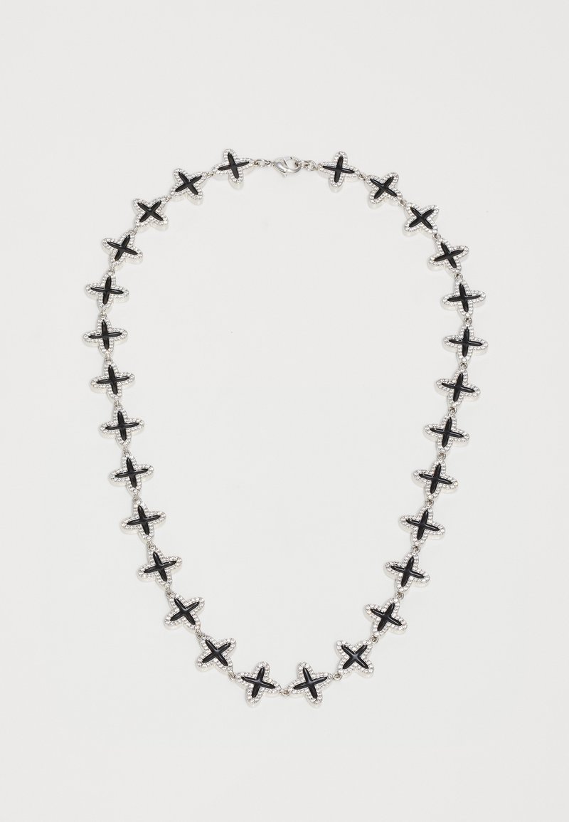 Stříbrný řetízek s rovnoměrně rozloženými černými křížovými články na bílém pozadí, s uzávěrem na sponu typu langusta.