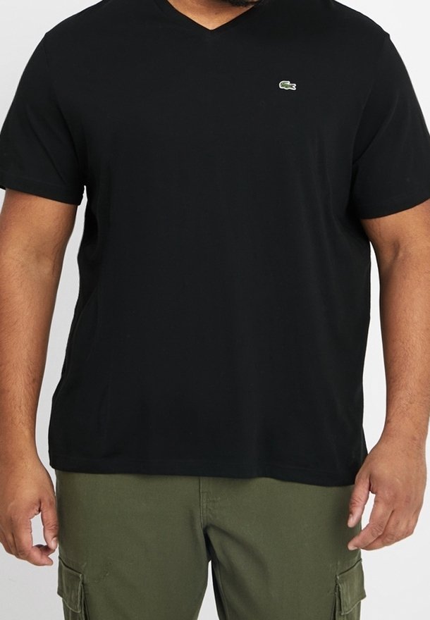 Homme portant un t-shirt noir à col en V et manches courtes, ainsi qu'un pantalon cargo vert olive, debout les bras détendus le long du corps.