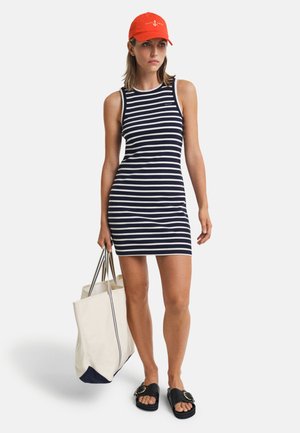 Abito senza maniche a righe blu navy e bianche, sandali neri con fibbia, cappellino arancione e borsa crema con rifiniture blu scuro.