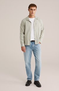 Svijetlozeleni košulja s dugim rukavima preko bijele majice, u kombinaciji s plavim trapericama i crnim cipelama. Košulja ima džep na prsima i ležeran kroj.