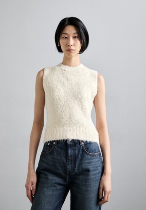 Knit sleeveless top in off-white with a textured finish, round neckline, and raw hem, paired with high-waisted blue jeans.