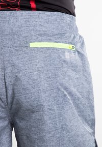 Šedé šortky s texturovanou tkaninou, které mají malou kapsu na zip s neonově zeleným zipem a nášivku s logem značky na zadní straně.