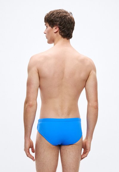 Μπλε μαγιό σλιπ με λείο ύφασμα, σχεδιασμό χαμηλής μέσης και μινιμαλιστικό στυλ. Χωρίς επιπλέον σχέδια ή μεταλλικά στοιχεία.