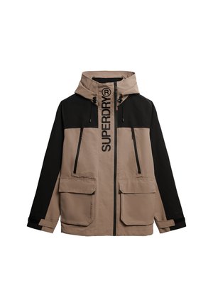 Farveblokeret jakke i beige og sort, med hætte, store forlommer og fed "SUPERDRY" logo langs den forreste lynlås.