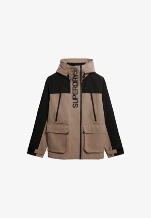 Kurtka w kolorze beżowym i czarnym z blokami kolorów, z kapturem, dużymi kieszeniami z przodu oraz wyraźnym logo "SUPERDRY" wzdłuż zapięcia.