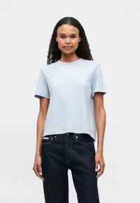 Ανοιχτό μπλε κοντομάνικο T-shirt με στρογγυλή λαιμόκοψη και ανάγλυφο λογότυπο. Φτιαγμένο από μαλακό βαμβάκι, συνδυασμένο με σκούρα τζιν.