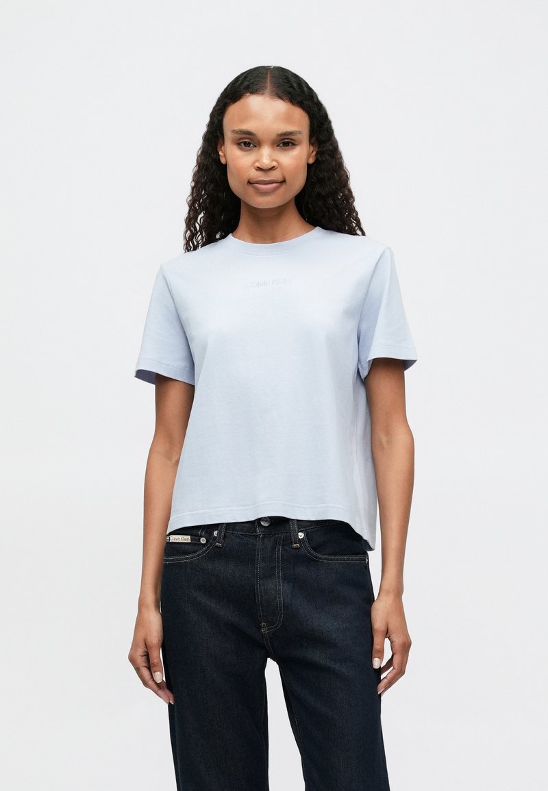 Ανοιχτό μπλε κοντομάνικο T-shirt με στρογγυλή λαιμόκοψη και ανάγλυφο λογότυπο. Φτιαγμένο από μαλακό βαμβάκι, συνδυασμένο με σκούρα τζιν.