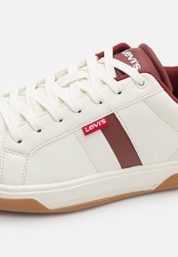 White sneakers with a maroon stripe, featuring a red Levi's logo, white laces, and a textured rubber sole. Smooth leather upper.