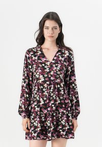 Robe florale avec un fond noir parsemé de fleurs roses et blanches, manches longues, décolleté en V et ourlet en étages. Texture de tissu douce.