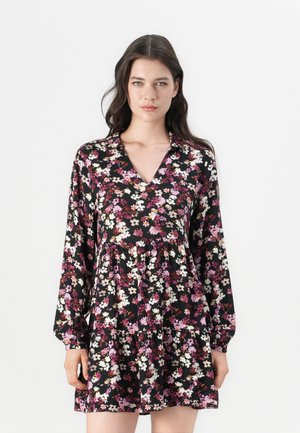 Robe florale avec un fond noir parsemé de fleurs roses et blanches, manches longues, décolleté en V et ourlet en étages. Texture de tissu douce.