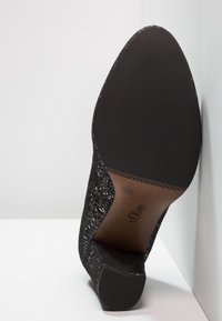 Chaussure à talon noire texturée inclinée vers le haut, montrant une semelle pointue avec la taille 37 et la marque "s.Oliver".