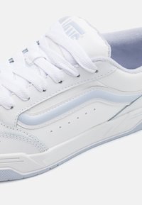 White athletic sneaker with blue accents, featuring a leather upper, textured laces, perforated detailing, and a rubber sole.