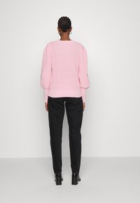 Maglione rosa a maglia con maniche a palloncino, texture a coste e orlo aderente, abbinato a pantaloni neri a sigaretta e stivaletti neri con tacco.