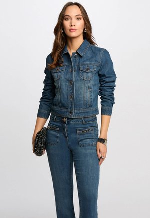 Veste en jean bleu foncé, avec deux poches poitrine, fermeture à boutons et poignets côtelés. Associée à un jean assorti et une pochette texturée.