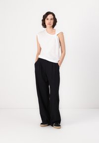 Hvit utenermet topp med draperingsdesign, kombinert med løse svarte bukser. Glatt tekstur, avslappet passform og vide ben.