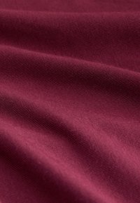 Close-up of soft, ribbed fabric in burgundy with gentle folds showing texture and weave pattern.