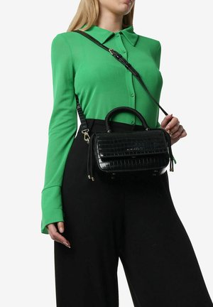 Borsa nera con motivo coccodrillo, dotata di doppi manici e tracolla rimovibile, presentata su una blusa verde e pantaloni neri.