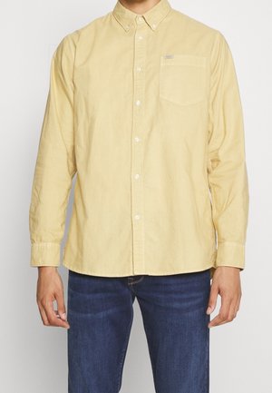 Chemise à manches longues, boutonnée, en coton jaune doux. Comprend une poche poitrine unique et un col classique avec des accents de boutons.