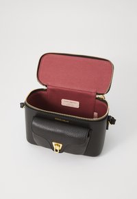 Black leather crossbody bag with textured surface, gold hardware, and a maroon interior. Features a zip closure and front pocket.