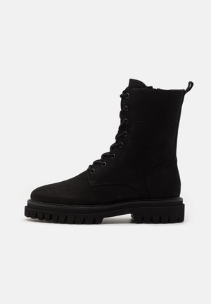 Stivali neri in suede con lacci, suola robusta, punta tonda, cuciture rinforzate e un'etichetta sul colletto per facilitarne l'indossamento.