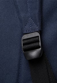 Correa de tela navy con superficie texturizada y hebilla de plástico negro, que presenta un detalle de costura triangular en el punto de sujeción.