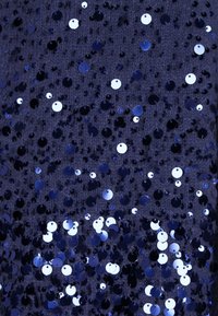 Tessuto navy ricoperto da numerosi paillette rotonde e lucide in diverse sfumature di blu, che riflettono la luce con uno strato sottostante dalla texture evidente.
