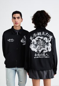 Črna jakna z zadrgo z grafičnimi oblikami spredaj in zadaj; podrobne bele ilustracije in japonsko besedilo; gladek material; sproščen kroj.