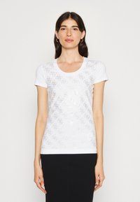 Hvid kortærmet t-shirt med et diskret, sølvfarvet logomønster over hele stoffet og rund halsudskæring. Materialet virker glat og let.