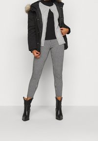 Svart parkas med pälskant, grå lager-på-lager topp och svarta hounds-tooth leggings. Avslutad med svarta ankelstövlar, elegant design och skräddarsydd silhuett.