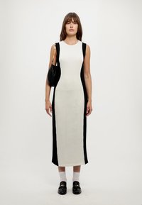 Abito midi senza maniche con pannello anteriore bianco e pannelli laterali neri, realizzato in tessuto morbido, abbinato a una borsa nera e mocassini.