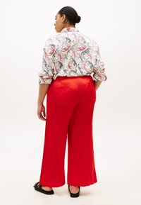 Κόκκινο παντελόνι φαρδιάς γραμμής με λεία υφή, που διαθέτει δύο πίσω τσέπες. Συνδυάζεται με πουκάμισο με σχέδιο σε αποχρώσεις λευκού, μπλε και ροζ.