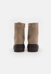 Stivaletti beige in pelle con chiusura a zip, punta arrotondata e suola in gomma marrone scuro. Superficie strutturata con dettagli di cucitura minimi.