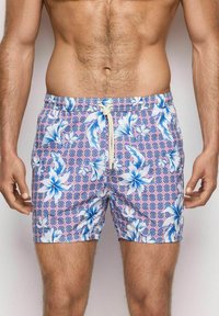 I pantaloni da nuoto con un motivo floreale presentano fiori bianchi e blu su uno sfondo geometrico rosa. Vita regolabile con cordino e tessuto leggero.