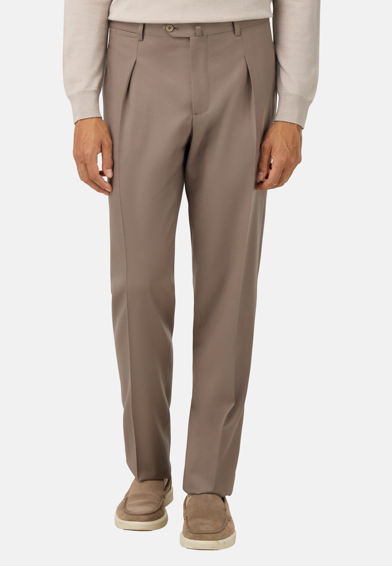 Beiga herrbyxor med veck, i kombination med ljusbruna slip-on skor och en beige långärmad topp, visade från midjan till fötterna mot vit bakgrund.