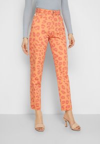 Calças cor pêssego com um padrão de estampa de leopardo, design de cintura alta e corte reto, combinadas com sapatos de tacão aberto bege.