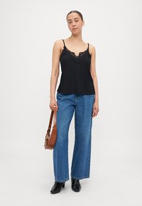 Černý top s krajkovým lemem, volné modré džíny, černé kotníkové boty a hnědá crossbody taška, na jednoduchém světlém pozadí.