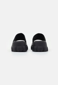 Zapatos negros de slip-on con suela gruesa y texturizada. Presentan un material suave y un diseño de parte trasera abierta para facilitar su uso.