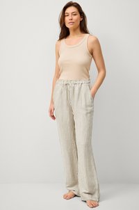 Top in cotone beige a costine abbinato a pantaloni ampi a righe chiare con vita elastica e cordoncino. La modella è in piedi a piedi nudi.