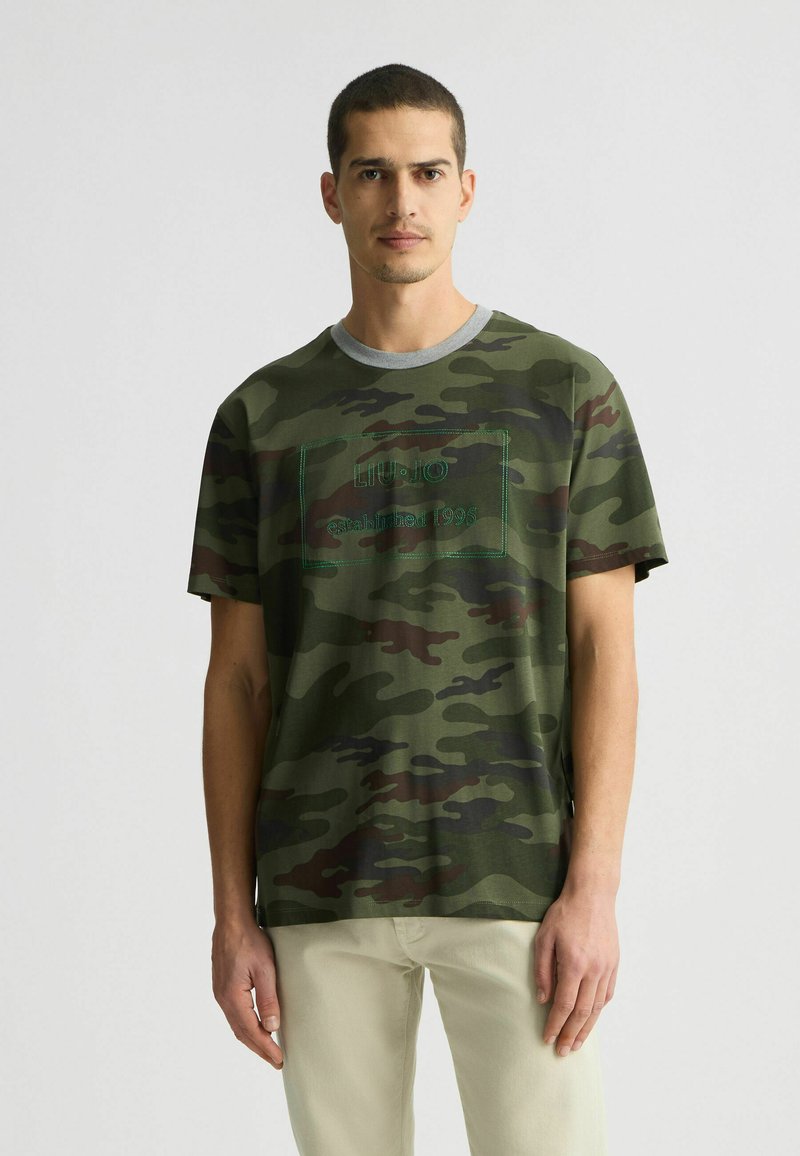 Roheline camo lühikeste varrukatega T-särk halli ümarikaelusega, mille esiosas on tikandiga tekst "LIU•JO asutatud 1995". Pehme kangast tekstuur.