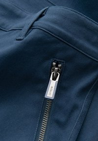 Gros plan sur un tissu bleu foncé avec un curseur de fermeture éclair argenté portant l'étiquette « ombre » sur une couture de poche.