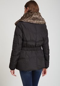 Svart puffjacka med krage i fuskpäls, bälte i midjan och sömnad på ryggen. Har en slät yta och en figurnära silhuett.