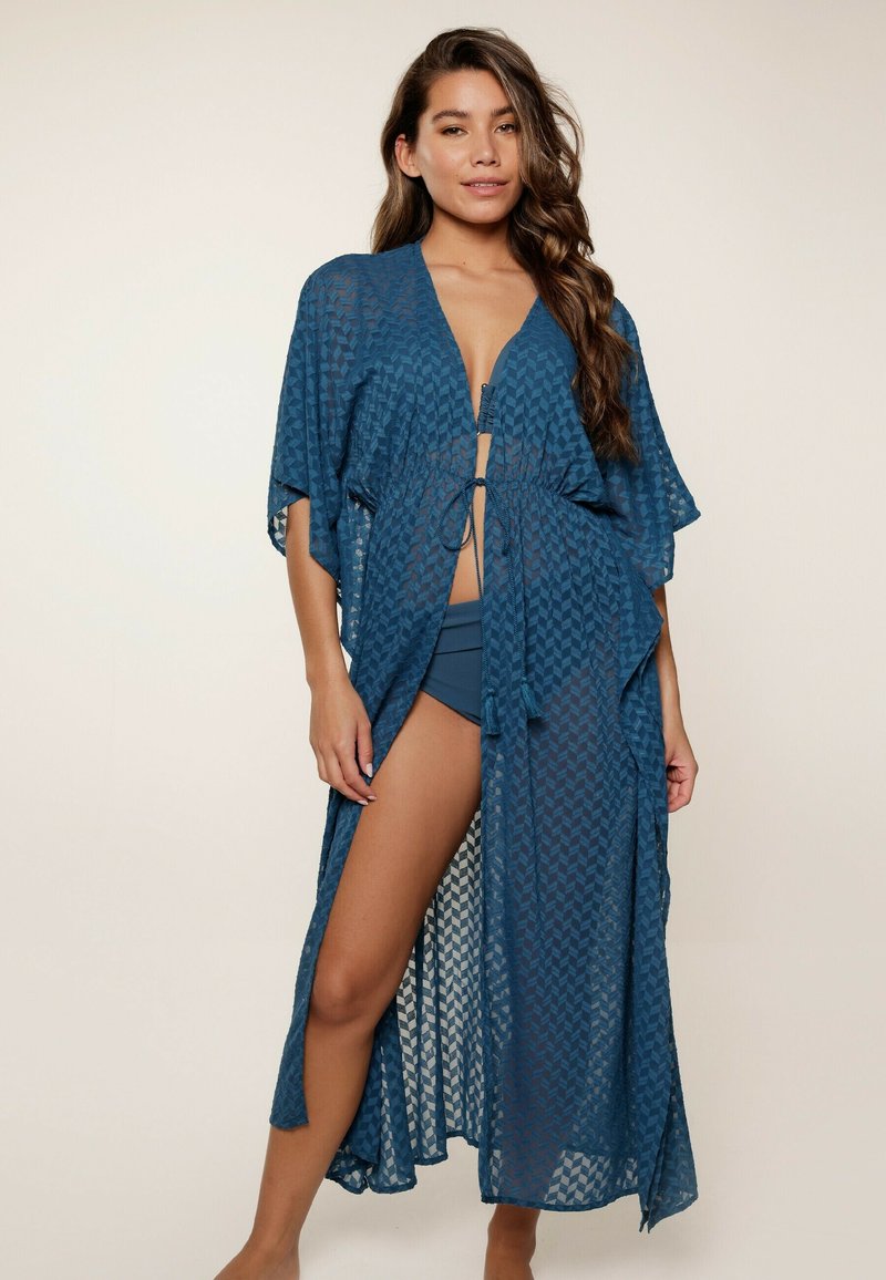 Kaftan blu, a fantasia, con maniche corte e vita regolabile, realizzato in tessuto leggero. Presenta una lunga apertura frontale e spacchi laterali.