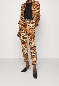 Tijger gestreepte blazer en bijpassende broek in oranje en zwart; zachte stof met zakken; gecombineerd met zwarte hakken mules.