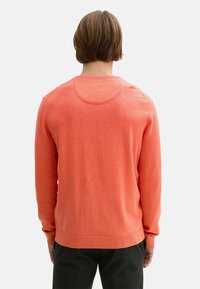 Pulover cu mânecă lungă în coral vibrant, textură tricotată, decolteu rotund, manșete și tiv cu model cusut, cu un design minimalist, văzut din spate.