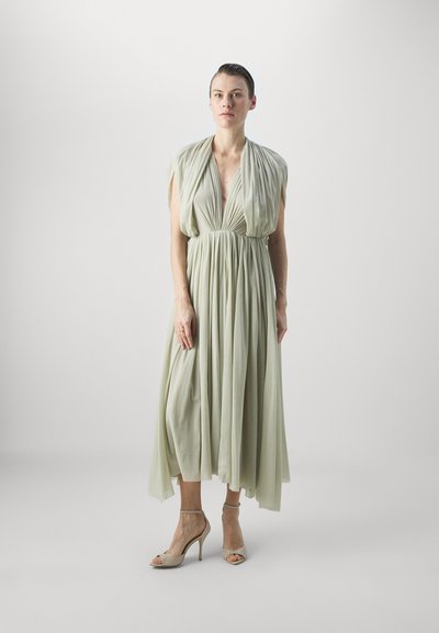 Rochie lungă, de un verde deschis, cu un corp drapat și talie strânsă. Realizată dintr-un material moale și fluid. Asortată cu sandale cu toc înalt bej.