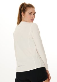 Langärmliges Sportoberteil in hellbeige mit strukturiertem Design und kontrastierendem Saum, mit reflektierenden Akzenten auf der Rückseite.