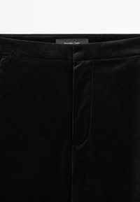 Gros plan sur la ceinture d'un pantalon en velours noir avec des coutures discrètes et une fermeture avant cachée.